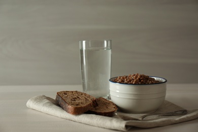 Photo of Buckwheat porridge, bread and glass of water on white wooden table. Fasting meals for Lent season