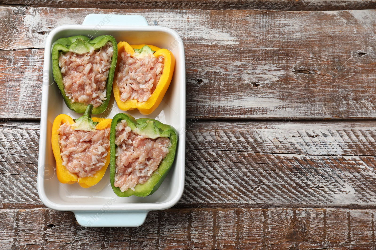 Photo of Raw stuffed peppers in dish on wooden table, top view. Space for text