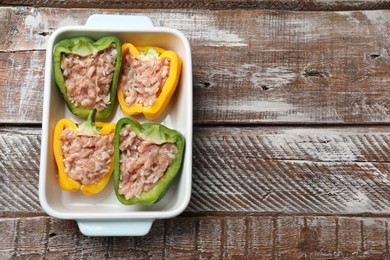 Raw stuffed peppers in dish on wooden table, top view. Space for text