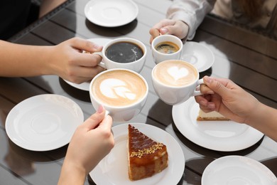 Photo of Friends drinking coffee at wooden table in outdoor cafe, closeup