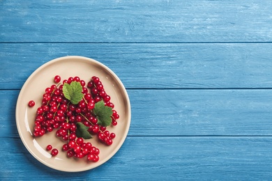 Photo of Delicious red currants and leaves on blue wooden table, top view. Space for text