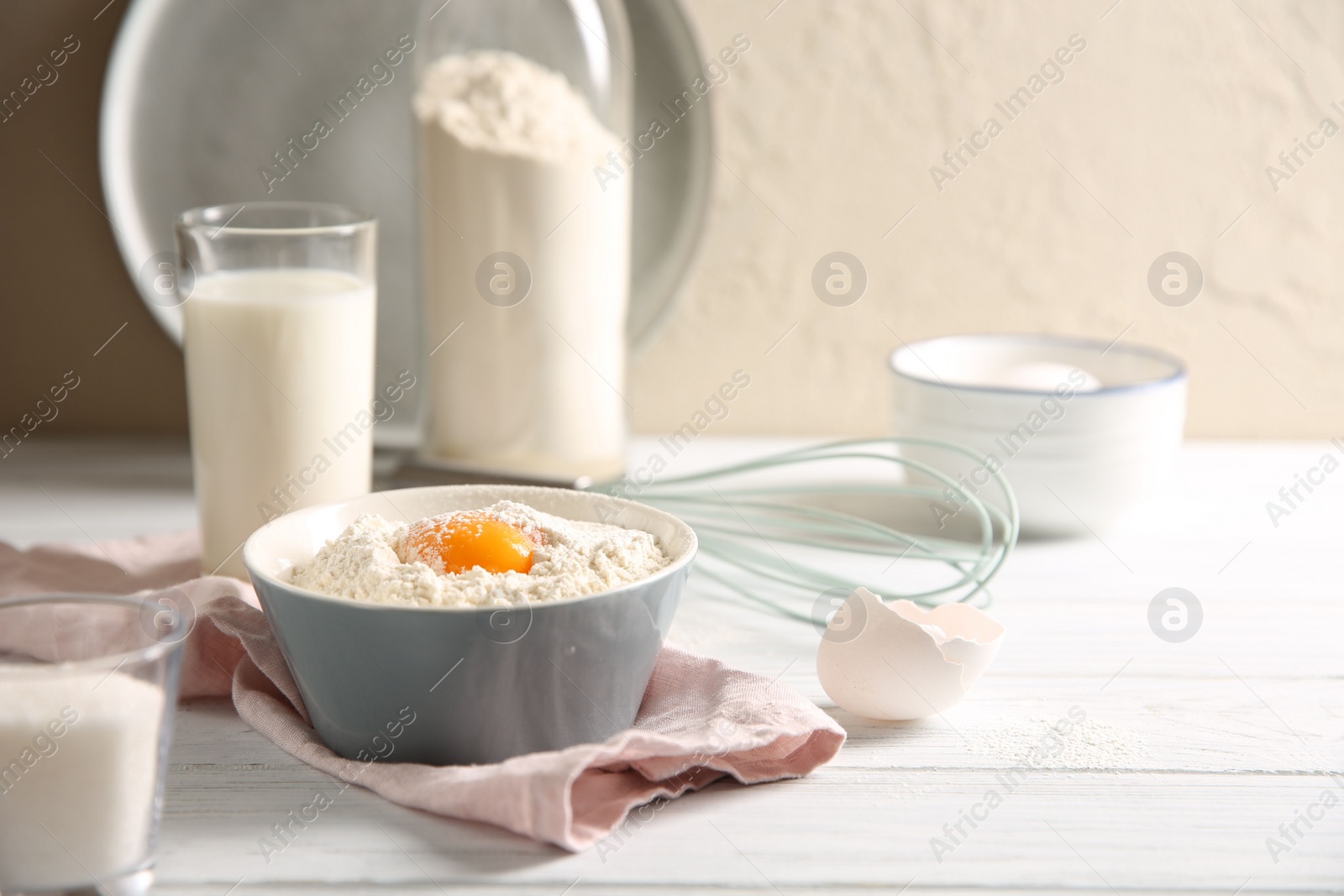 Photo of Making dough. Flour with yolk in bowl on white wooden table. Space for text