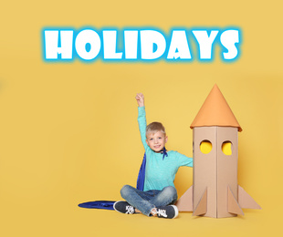 Image of School holidays. Cute little child playing with cardboard rocket near yellow wall