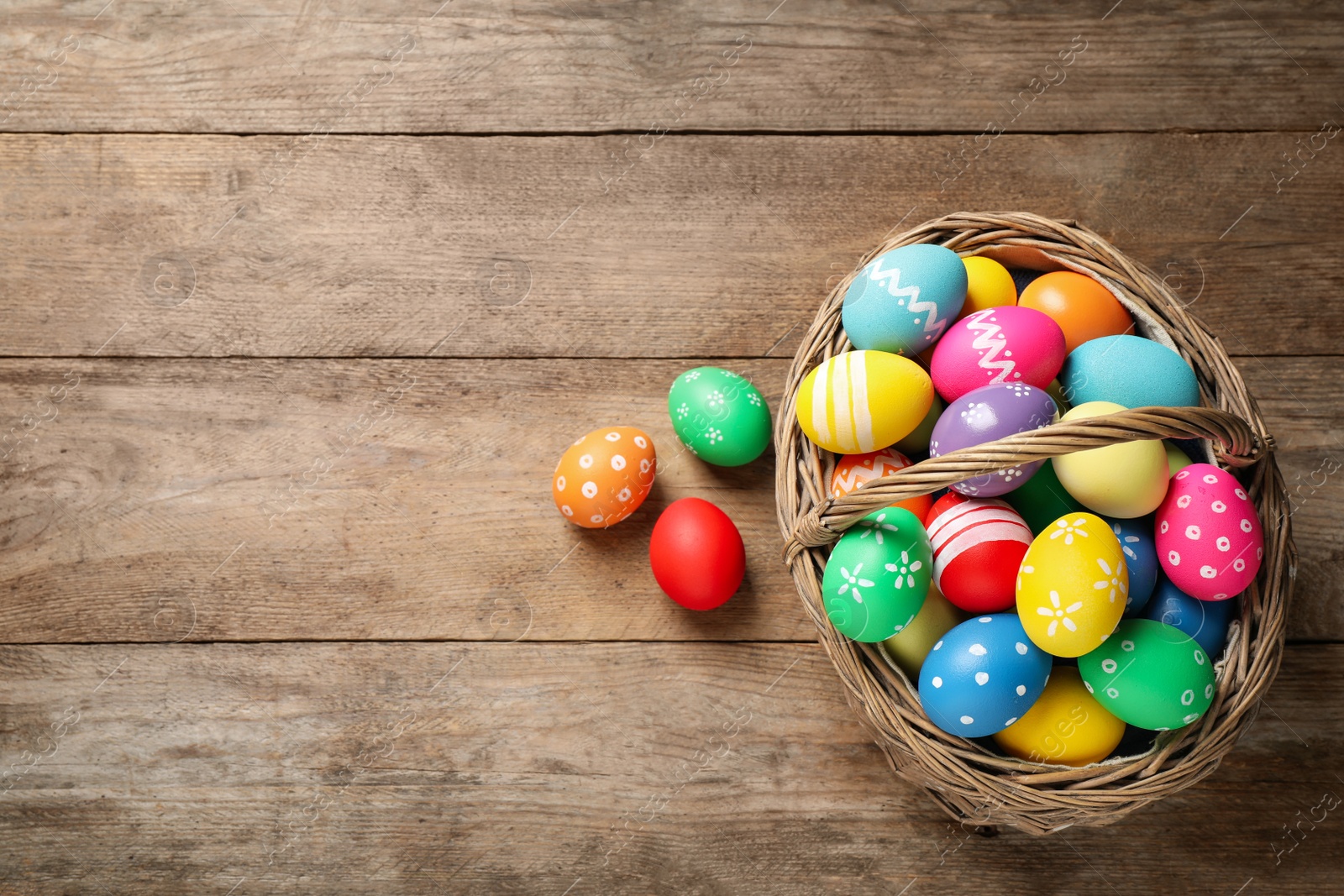 Photo of Colorful Easter eggs in basket on wooden background, flat lay. Space for text