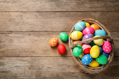 Photo of Colorful Easter eggs in basket on wooden background, flat lay. Space for text