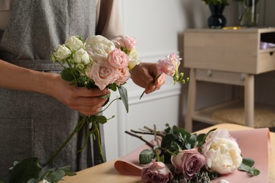 Florist creating beautiful bouquet at wooden table indoors, closeup