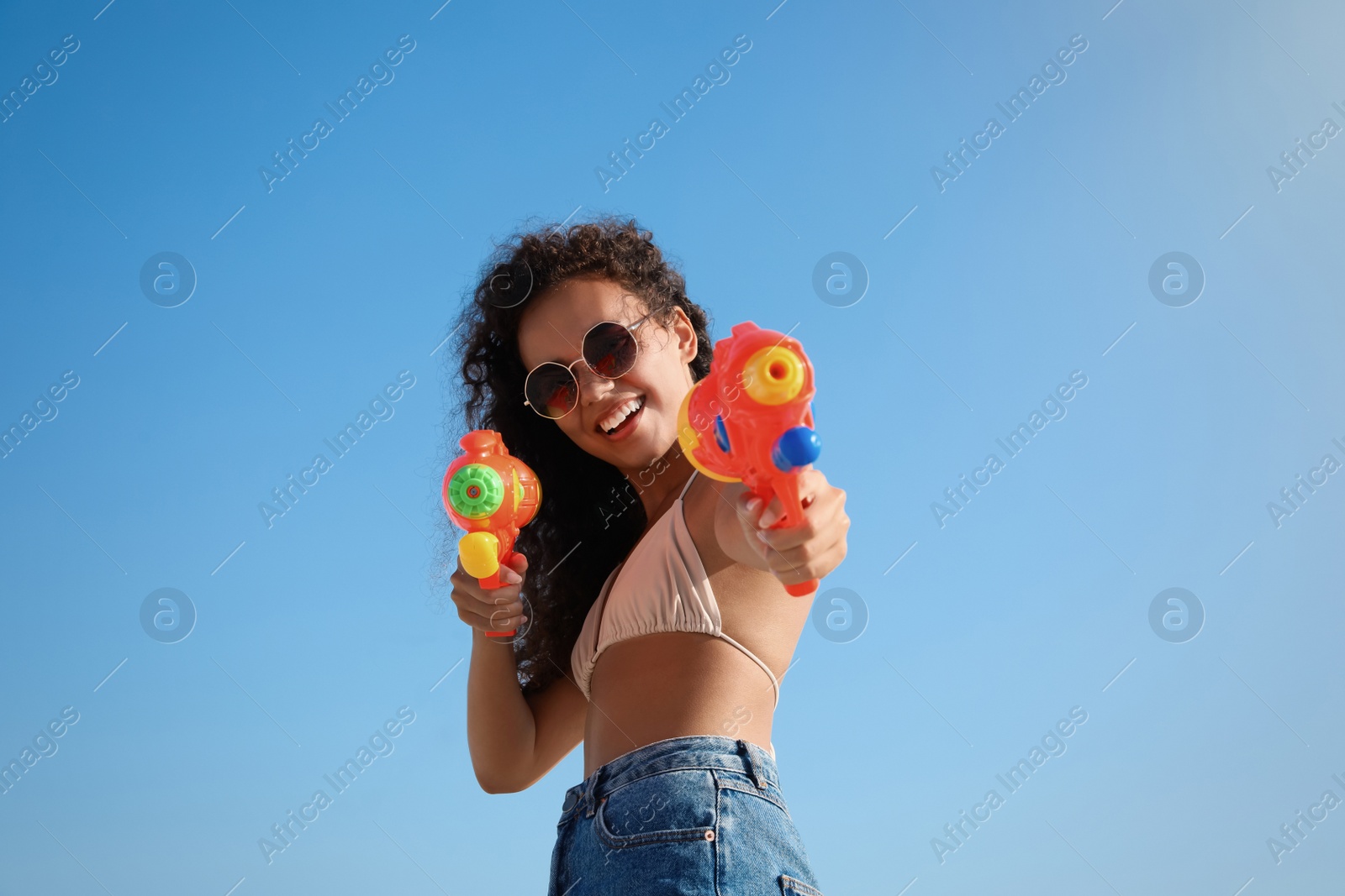 Photo of African American woman with water guns having fun against blue sky