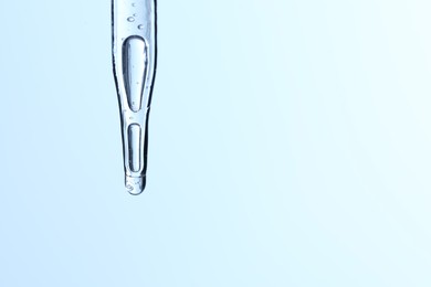 Photo of Dripping liquid from pipette on light blue background, closeup. Space for text