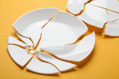 Two broken ceramic plates on orange background, closeup