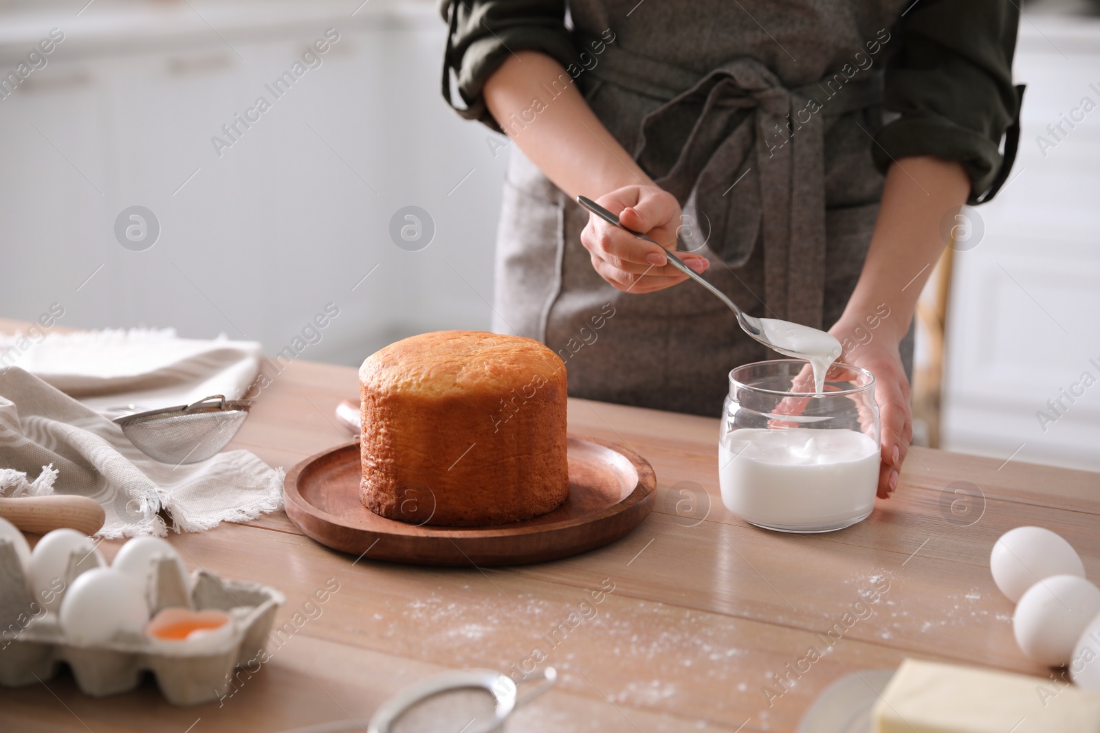 Photo of Young woman decorating traditional Easter cake with glaze in kitchen, closeup