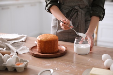 Photo of Young woman decorating traditional Easter cake with glaze in kitchen, closeup