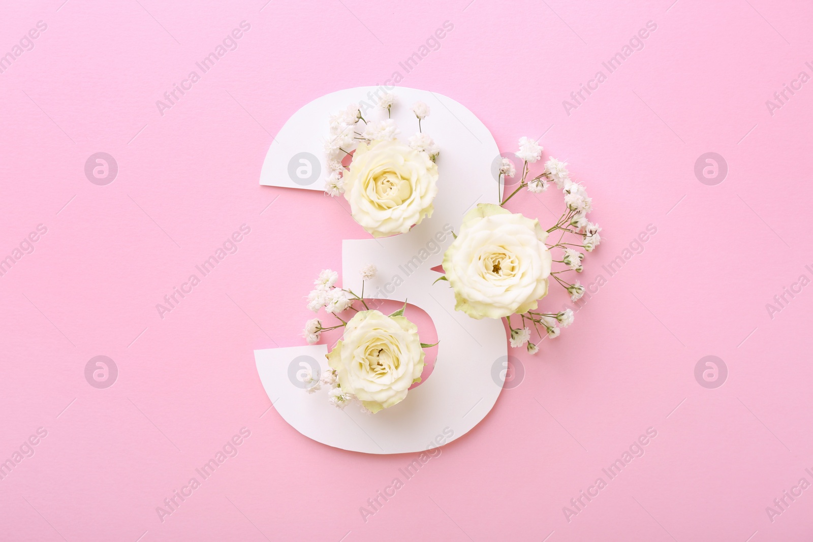 Photo of Paper number 3 and beautiful flowers on pink background, top view