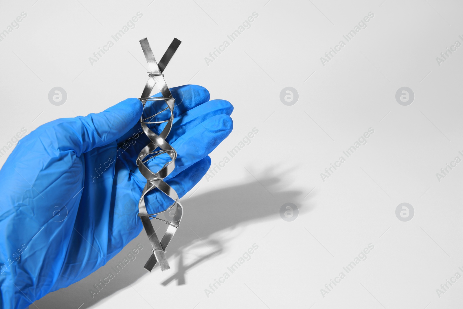 Photo of Scientist with DNA molecular chain model made of metal on white background, closeup. Space for text