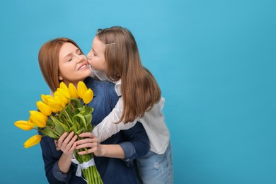 Mother and her cute daughter with bouquet of yellow tulips on light blue background. Space for text
