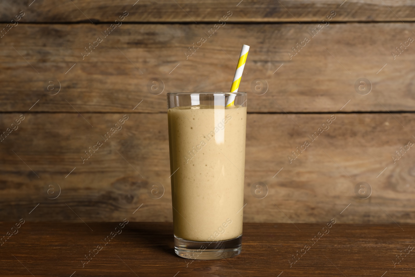 Photo of Glass of tasty smoothie with straw on wooden table