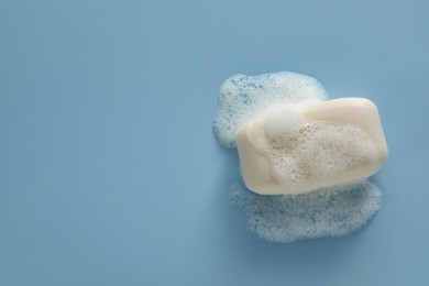 Photo of Soap bar with fluffy foam on light blue background, top view. Space for text