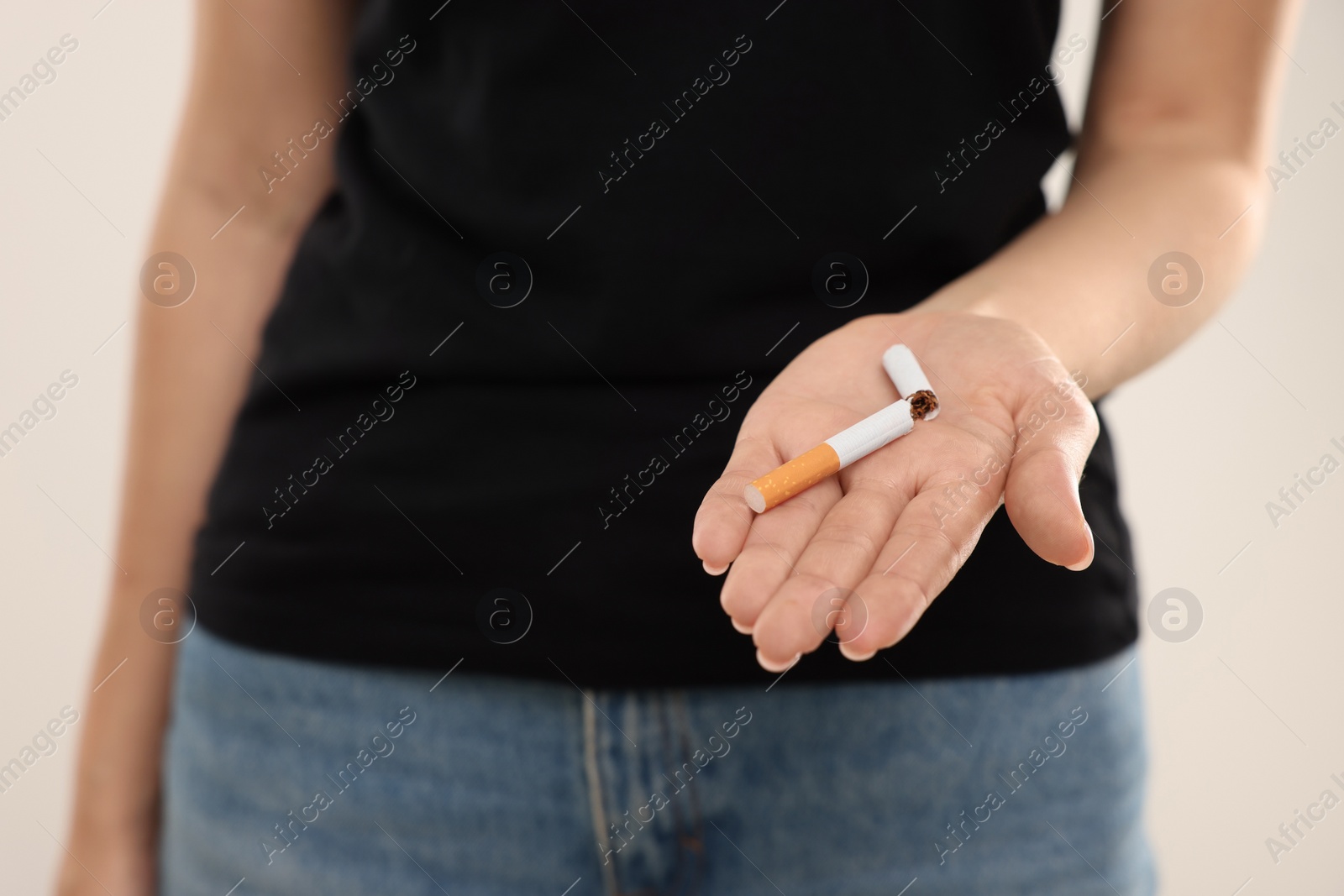 Photo of Stop smoking concept. Woman holding broken cigarette on beige background, closeup