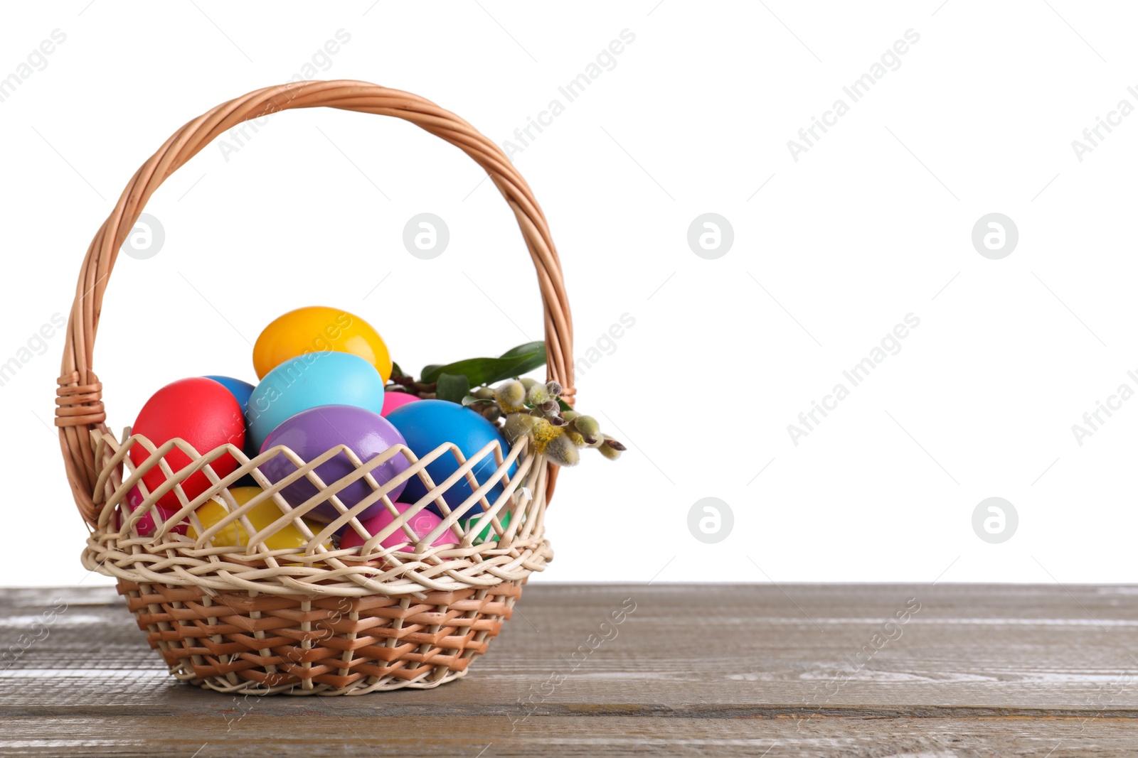 Photo of Colorful Easter eggs in wicker basket on wooden table against white background