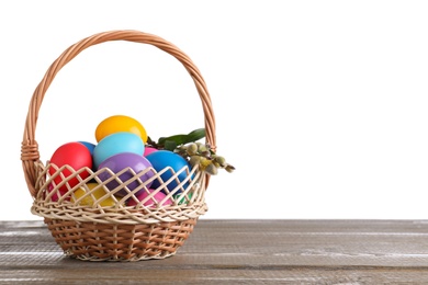 Photo of Colorful Easter eggs in wicker basket on wooden table against white background