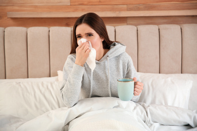 Photo of Sick young woman with cup of hot drink in bed at home. Influenza virus