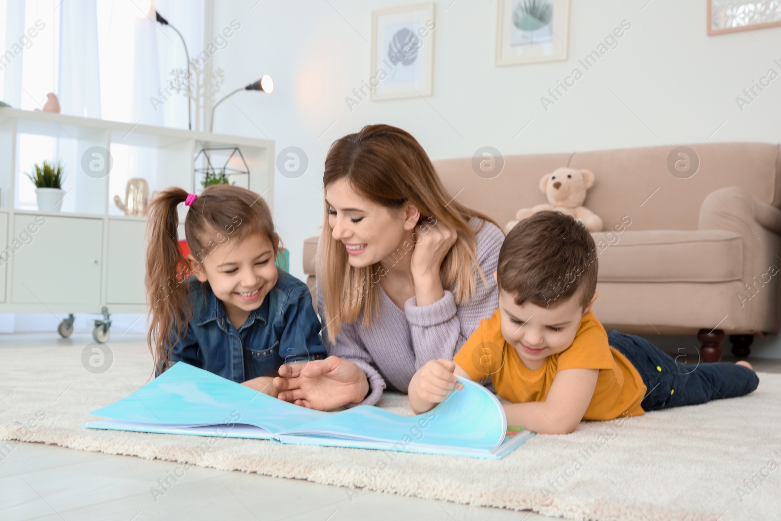 Photo of Little children with their nanny lying on floor and reading book at home