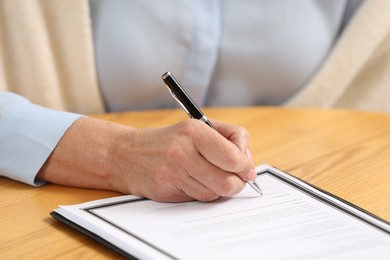 Senior woman signing Last Will and Testament at wooden table, closeup