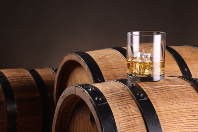 Whiskey with ice cubes in glass on wooden barrel against dark background