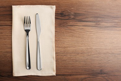 Photo of Shiny fork, knife and napkin on wooden table, top view. Space for text