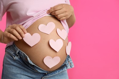Photo of Pregnant woman with heart shaped sticky notes on belly against pink background, closeup. Choosing baby name