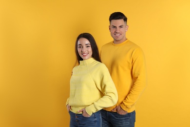 Happy couple wearing warm sweaters on yellow background