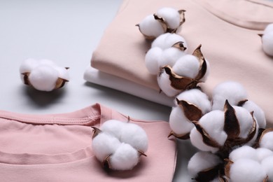Photo of Cotton branch with fluffy flowers and t-shirts on light gray background, closeup