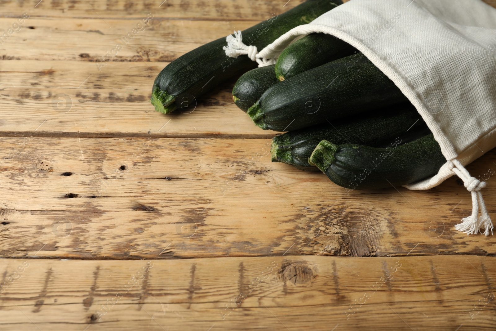 Photo of Sack with green ripe zucchinis on wooden table. Space for text