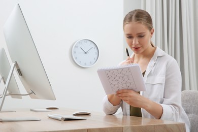 Photo of Young woman solving sudoku puzzle at workplace in office