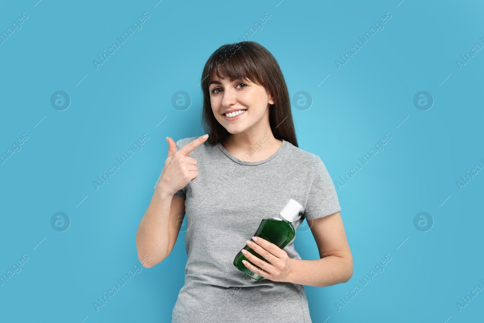 Photo of Young woman with mouthwash pointing at healthy teeth on light blue background