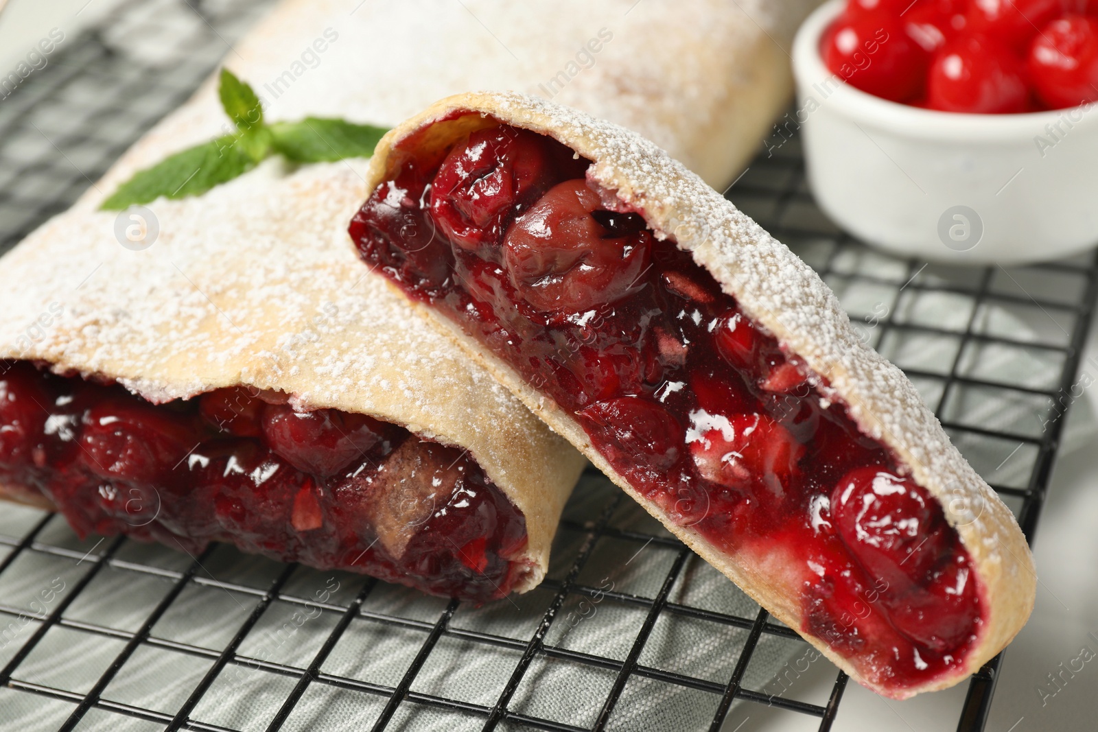 Photo of Delicious strudel with cherries on cooling rack, closeup