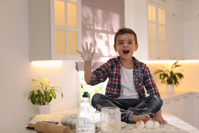 Photo of Emotional little boy with flour on face in kitchen. Cooking dough