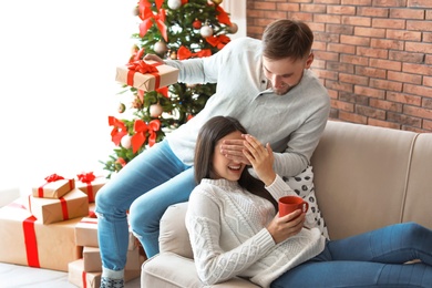 Young man surprising his girlfriend with Christmas gift at home