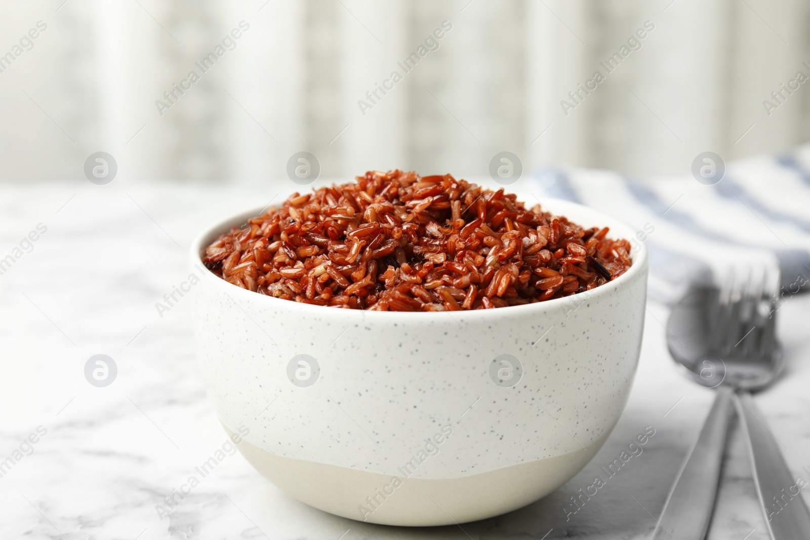 Photo of Bowl with delicious cooked brown rice on white marble table indoors