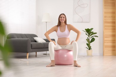 Photo of Pregnant woman sitting on fitness ball in room. Home yoga