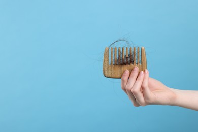 Photo of Woman holding comb with lost hair on light blue background, closeup and space for text. Alopecia problem