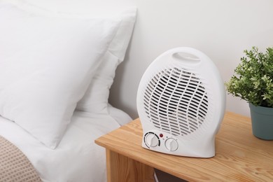 Modern electric fan heater on bedside table indoors
