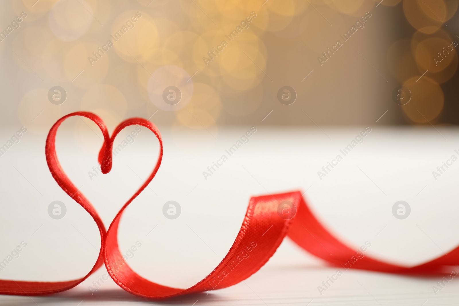 Photo of Heart made of red ribbon on table against blurred festive lights, space for text. Valentine's day celebration