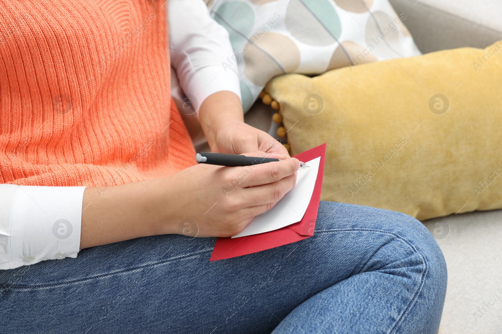 Photo of Young woman writing message in greeting card on sofa, closeup