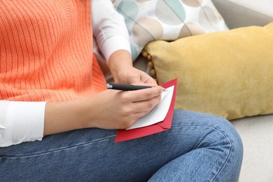 Young woman writing message in greeting card on sofa, closeup