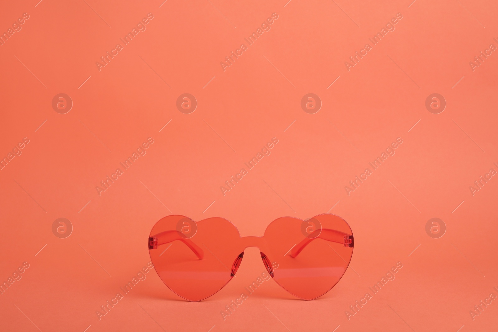 Photo of Heart shaped coral sunglasses on orange background. Space for text