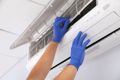 Photo of Professional technician maintaining modern air conditioner indoors, closeup