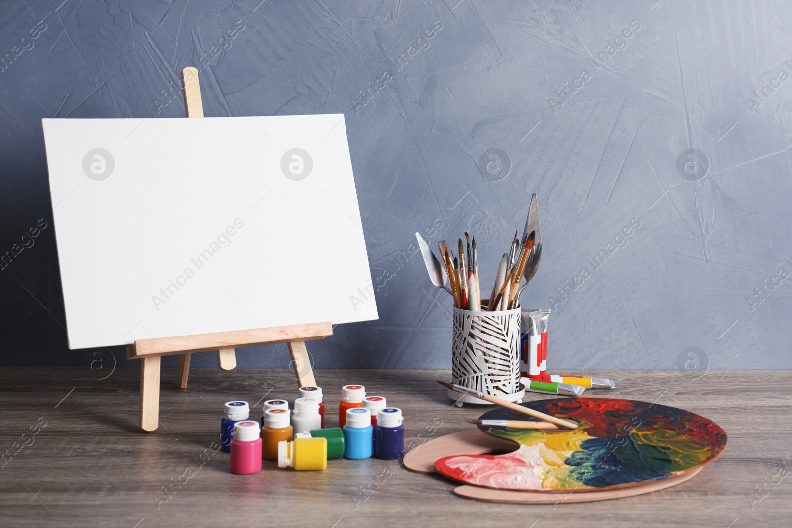 Photo of Easel with various artist tools on table against color wall. Space for text