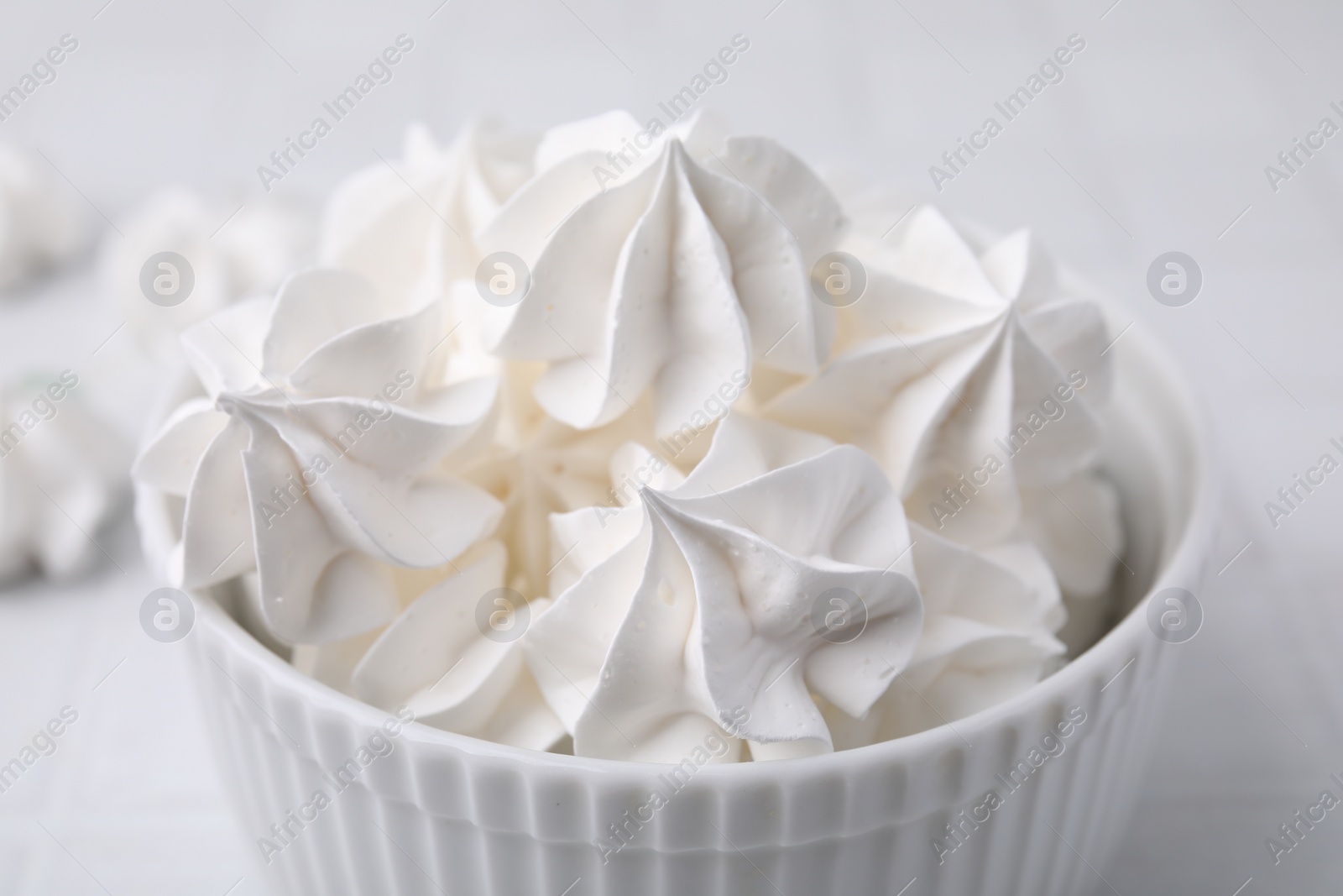 Photo of Delicious meringue cookies in bowl on white table, closeup