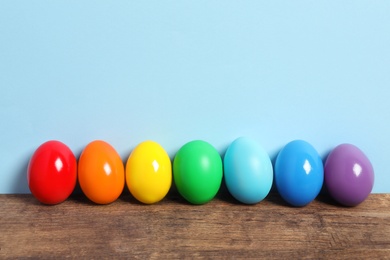 Photo of Easter eggs on wooden table against light blue background, space for text