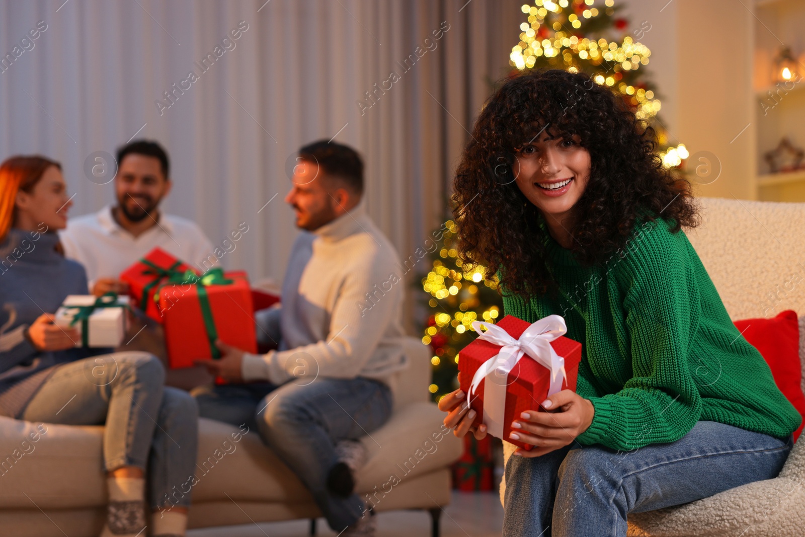 Photo of Christmas celebration in circle of friends. Happy young woman with gift box at home, selective focus